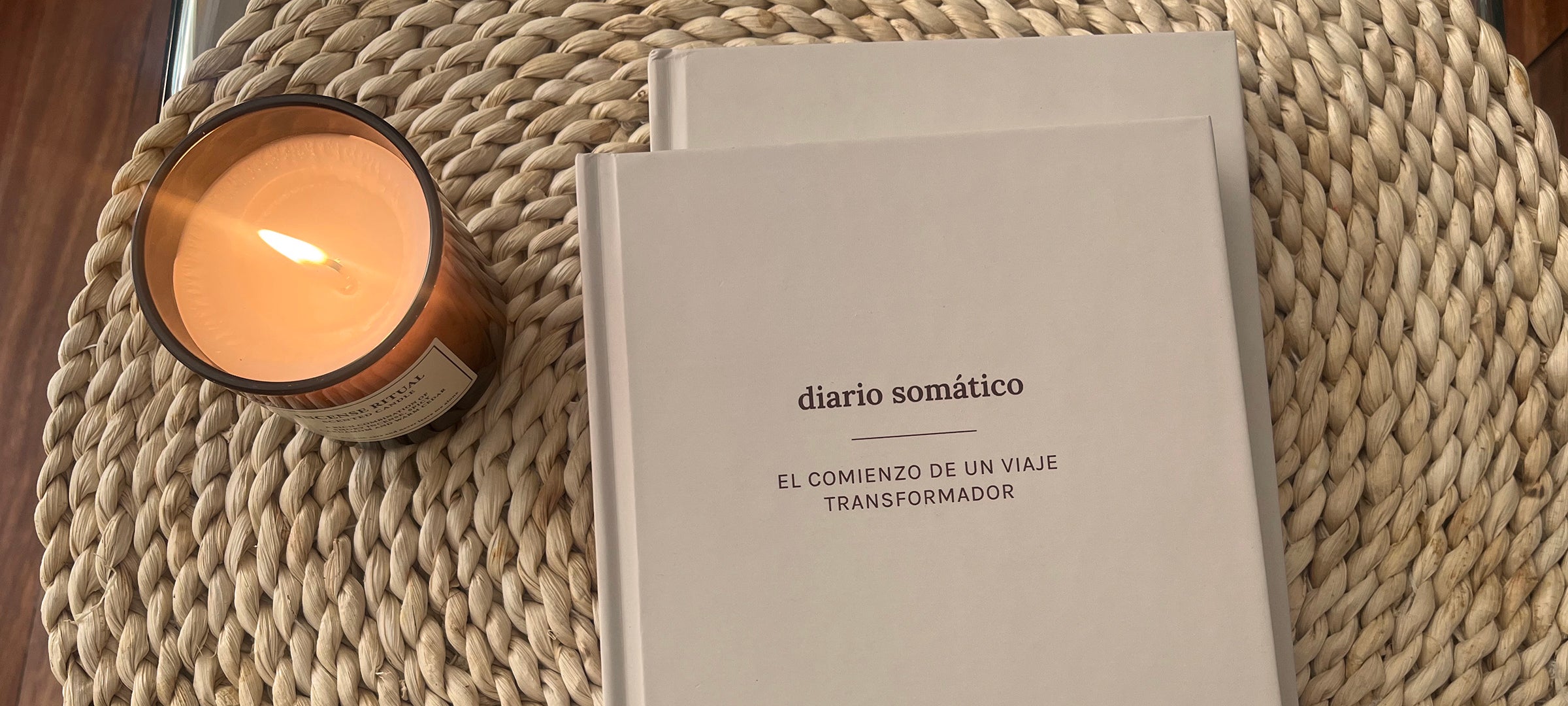 Diario somático junto a una vela encendida sobre una superficie natural, símbolo de autocuidado y conexión corporal
