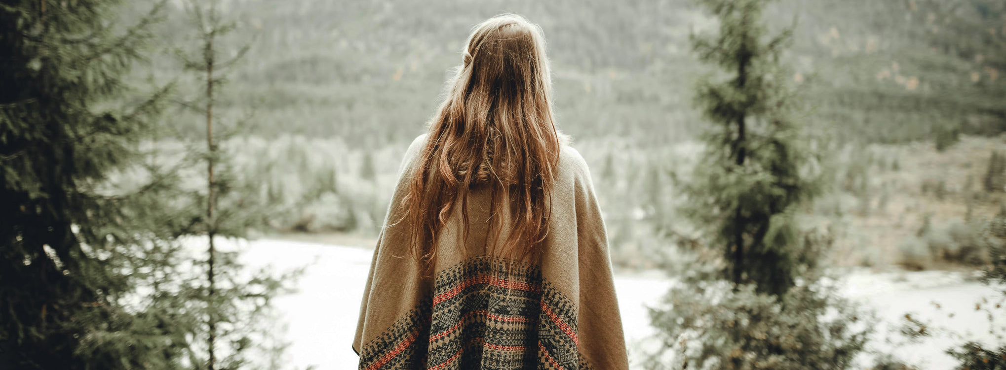 Mujer envuelta en un poncho de lana contemplando el bosque y la naturaleza, símbolo de introspección y conexión corporal